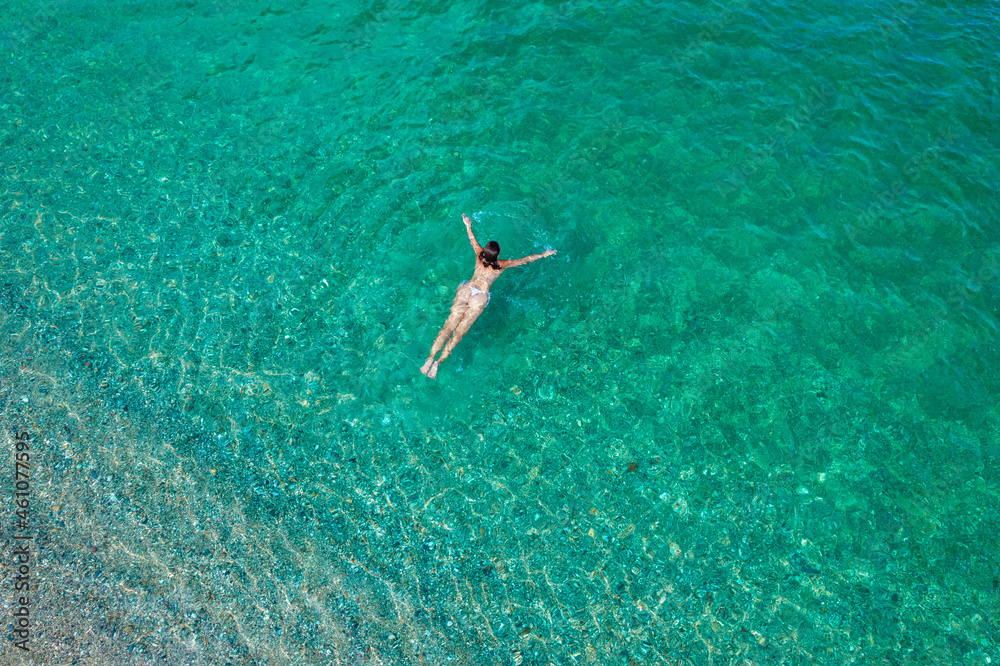 Young woman in a bikini swimming in sea water on the beach. View from ...