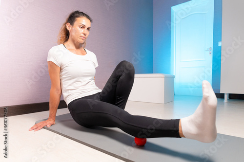 Athletic caucasian slim woman doing myofascial self-massage of the thigh and gluteus muscles in a massage room
