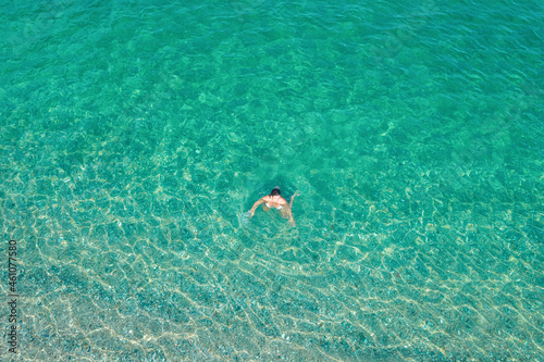 Young woman in a bikini swimming in sea water on the beach. View from above. Top, drone view © flowertiare