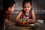 Little children looking at candles on cake and smiling at home party