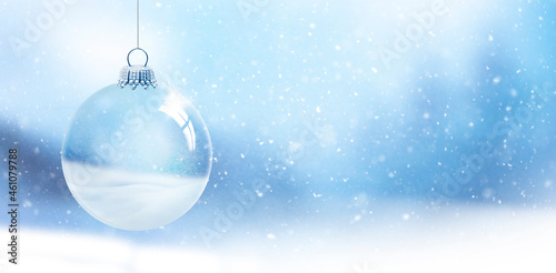 Gläserne Weihnachtskugel vor unscharfem Blauem Hintergrund mit Schneeflocken