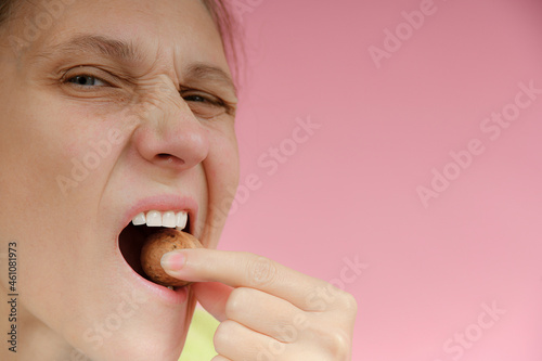 The girl holds a walnut in her teeth on a pink background. The concept of stamotology and proper nutrition.