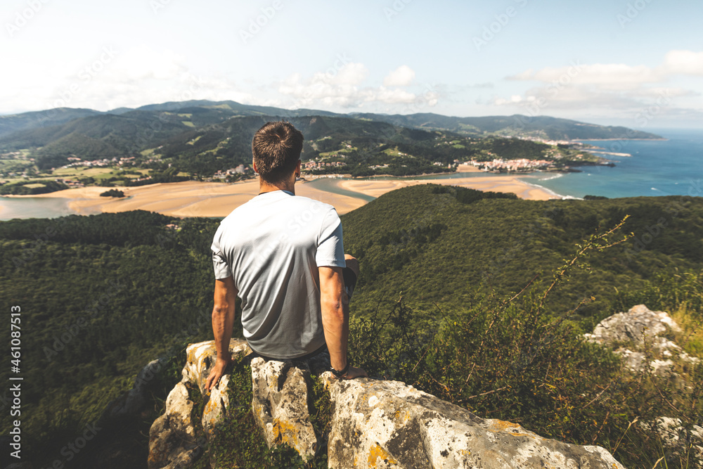 Fototapeta premium Young caucasian man on the top of a mountain looking to Urdaibai rivermouth next to the Cantabric sea, at Bizkaia; Basque Country.