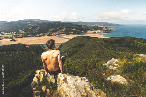Young caucasian shirtless man on the top of a mountain looking to Urdaibai rivermouth next to the Cantabric sea, at Bizkaia; Basque Country. photo