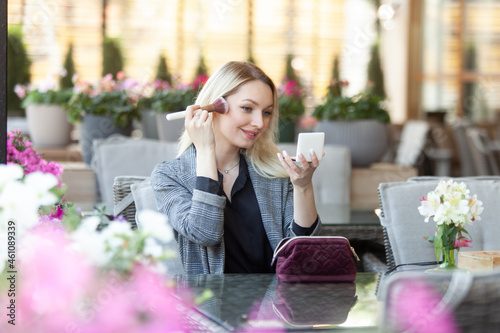 Young attractive beauty woman blonde applies a make-up with a make-up brush in summer terrace of cafe © splitov27