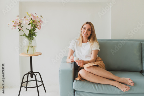 charming young woman with a cup of coffee sitting on the sofa at home