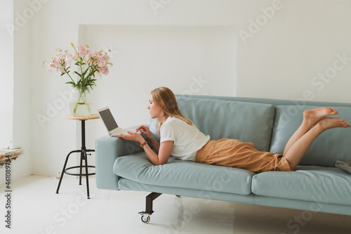 charming young woman with laptop working at home while sitting on sofa