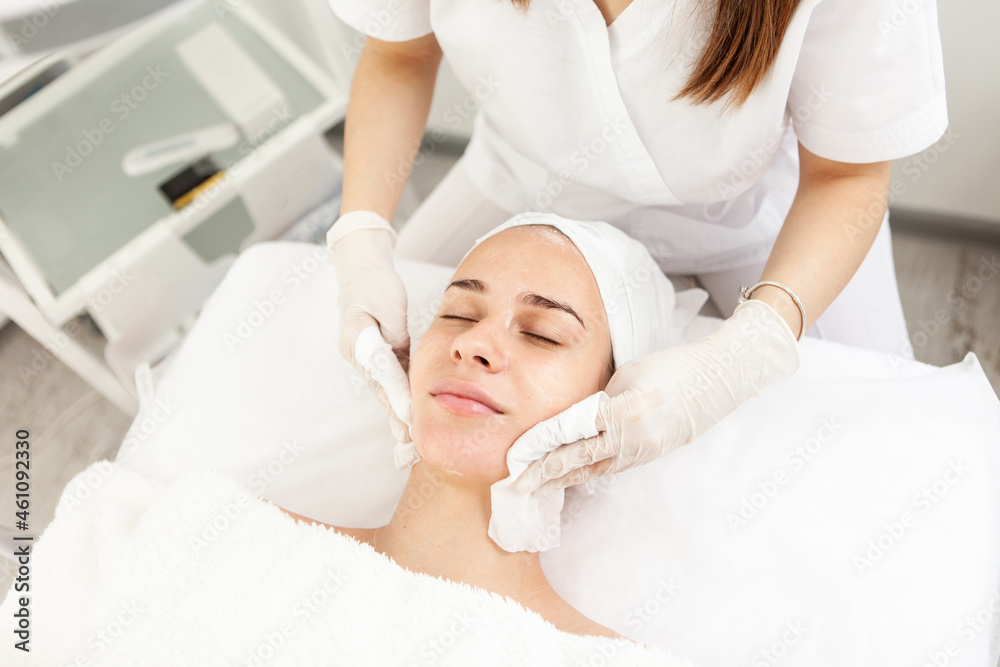 Facial massage and skincare treatment. Dermatologist hands cleaning relaxed serene young woman face with napkin in beauty salon during skincare treatment.