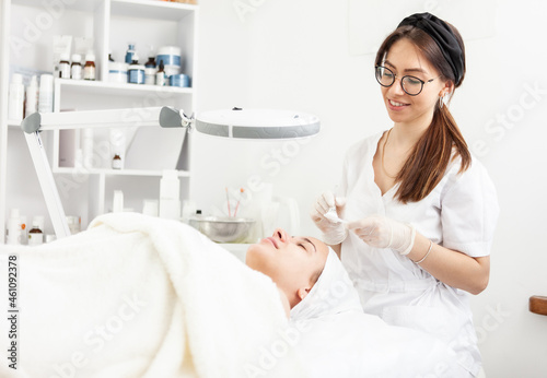 Cute woman beautician makes a cosmetic procedure to a patient in a beauty salon. Facial skin care