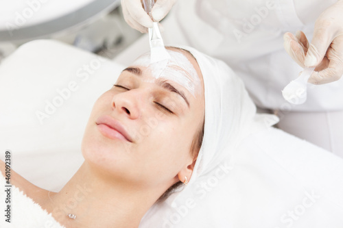 Beautician applies mask to beautiful feminine face in beauty salon. Facial hygiene, cosmetic procedures, skin care, skin pore cleansing, hardware cosmetology concept