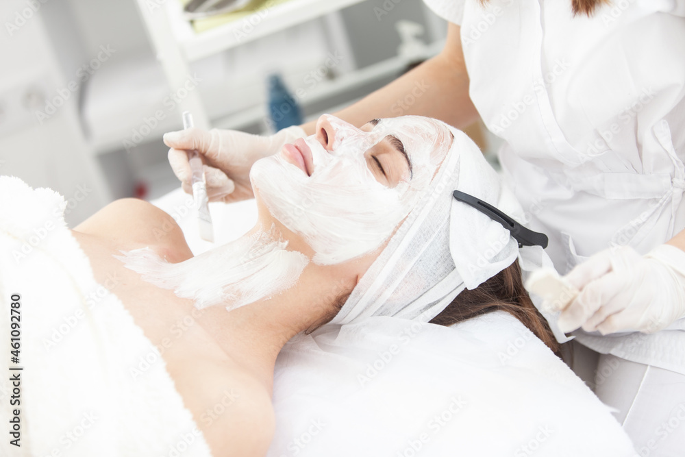 Fototapeta premium Cosmetological procedures. Beauty salon, doctor in gloves applies mask for beautiful woman with closed eyes with brush.