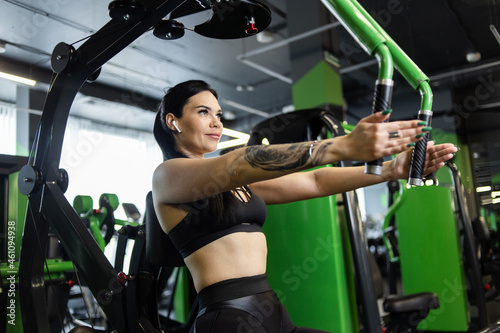 Young fitness woman exercising pectoral muscles doing hand reduction in exercise machine in gym