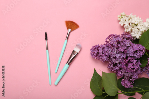 Makeup brushes with branches of blooming lilacs on pink background. Spring, beauty concept. Top view. Flat lay