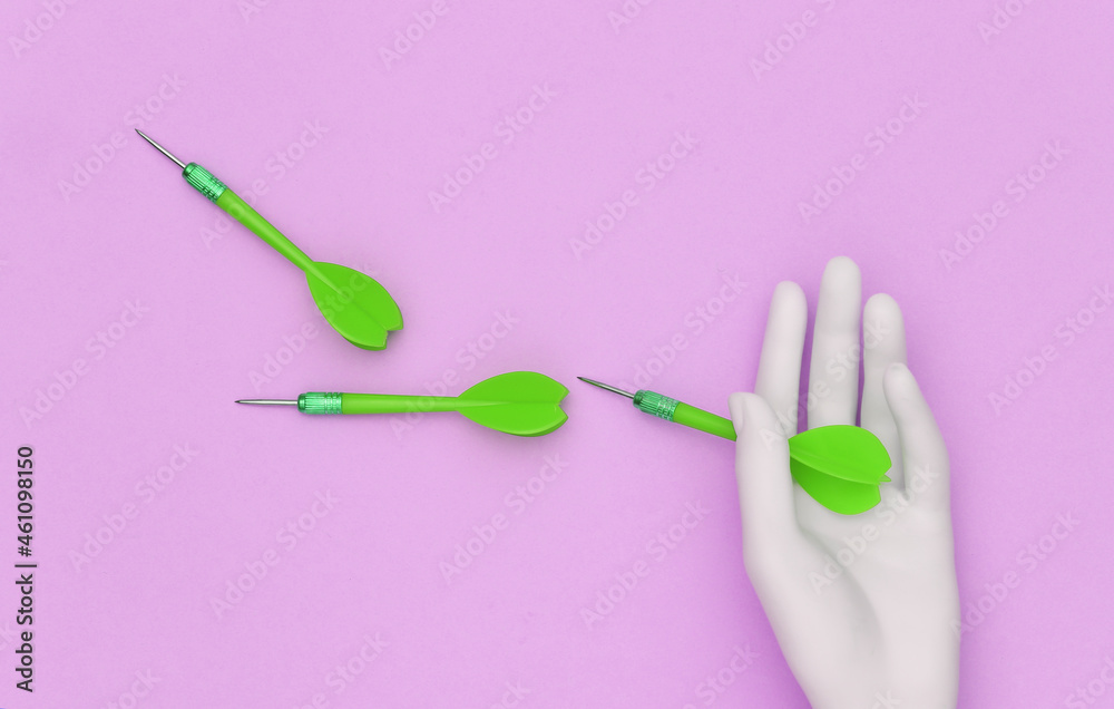 White mannequin hand holds dart needles on pink background. Top view White mannequin hand holds dart needles on pink background. Top view
