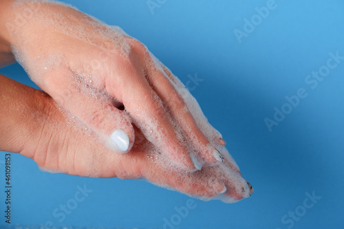 Bubble bath foam in woman s hands. Closeup woman s hand washing with soap on a blue background   selective focus. Practice good hygiene. Hygiene and health protection