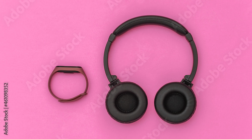 Wireless stereo headphones and smart bracelet on pink background. Modern gadgets. Top view