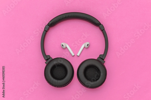 Wireless large stereo headphones and small earbuds on pink background. Top view