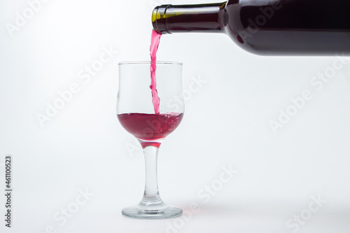 Red wine is poured into a glass from a bottle on a white background. Wine alcoholic drink.