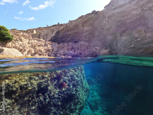 Underwater split photo of beautiful deep turquoise cave of Sykia a natural volcanic white chalk round shaped open top bay, Milos island, Cyclades, Greece