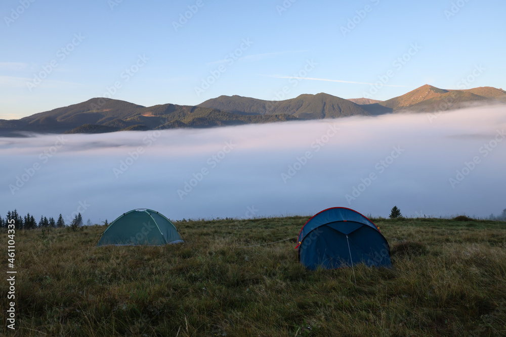 Picturesque mountain landscape with camping tents in foggy morning