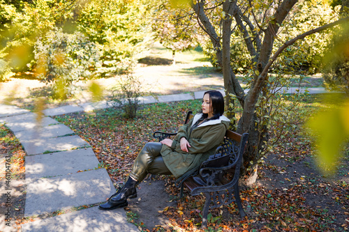 Young woman in park on sunny autumn day. Cheerful beautiful female in jacket with a hood outdoors on beautiful fall day