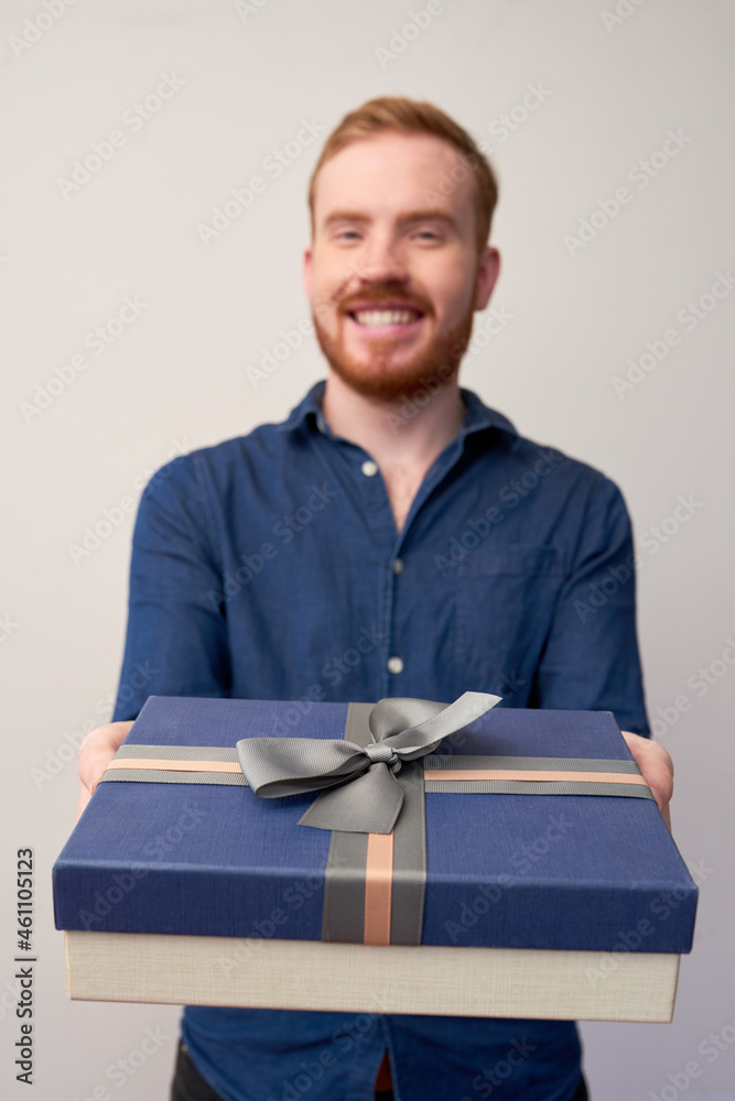 Portrait of happy young man giving dark blue gift box with bow to camera Portrait of happy young man giving dark blue gift box with bow to camera