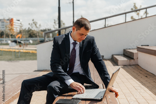A man in a business suit and a laptop sits on a bench. businessman with laptop.