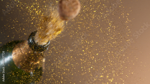 Freeze motion of champagne explosion with flying cork closure, opening champagne bottle closeup, golden bokeh glitters on background.