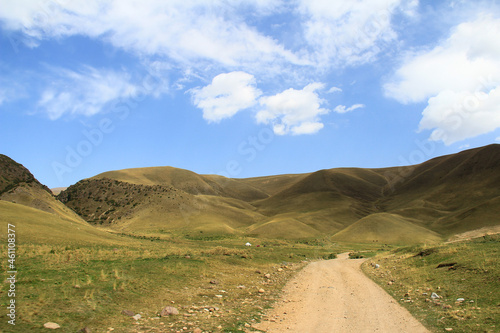 High yellow rounded mountains on the Assy plateau with a road, sky with clouds, summer, sunny