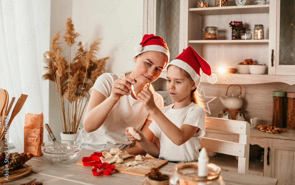 a little girl and mom in Christmas hats are sitting at the table and playing with flour