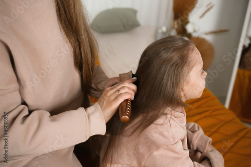 close-up of mom sitting on the bed and combing her daughter's hair