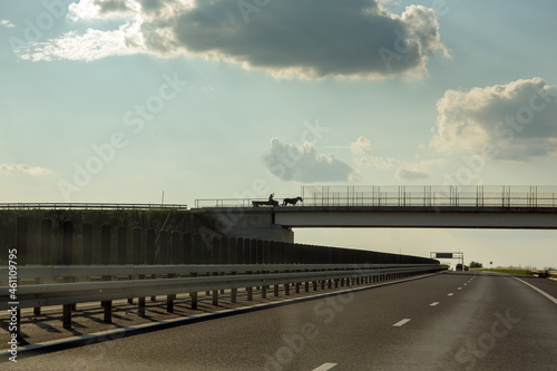 Wóz konny z ludźmi na moście nad autostradą na tle oświetlonego nieba z chmurami