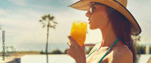 Valokuva Side profile cropped panoramic view face beautiful woman, wear straw hat hold glass drinks orange juice or cocktail refreshing at hot day relax on deckchair near pool