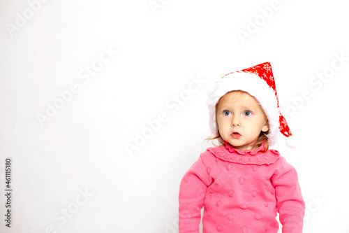 Portrait of a cute girl with blue eyes in a Christmas cap and a pink jumper. White background, space for text. New Year