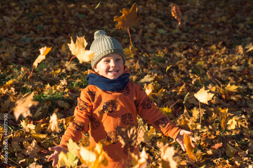 cute happy boy throwing autumn leaves outdoors sunny day