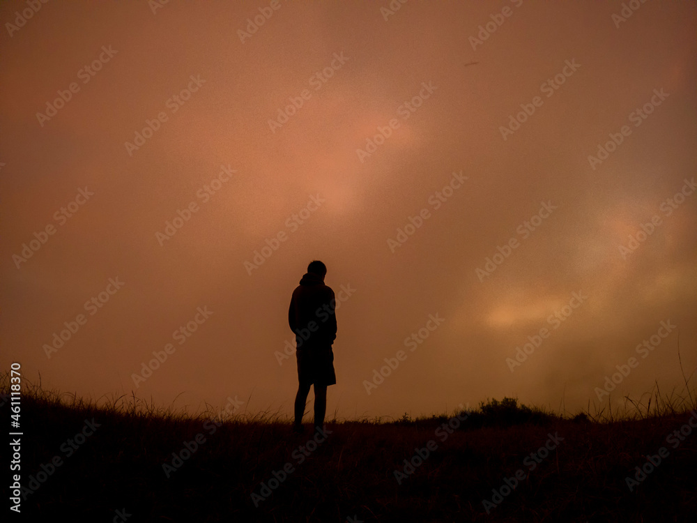 Silhouette of a camper watching the sunrise in the mist from top of 'Le Pouce' mountain located in Mauritius Silhouette of a camper watching the sunrise in the mist from top of 'Le Pouce' mountain located in Mauritius