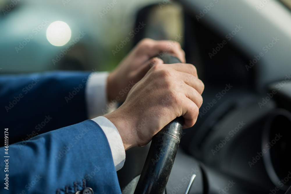 Close-up of a businessman holding a steering wheel of a car. Male hands in a blue suit on the steering wheel of a car.