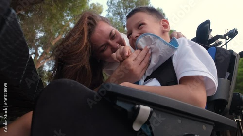 Loving mother feeling bond and love playing kissing on cheek her little 9s son with cerebral palsy sit in wheelchair outdoor photo