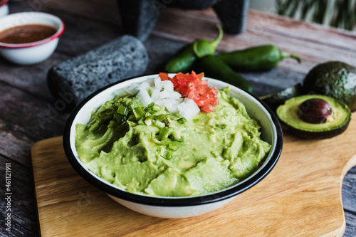 Bowl of Guacamole next to fresh ingredients on a wooden table in Mexico 