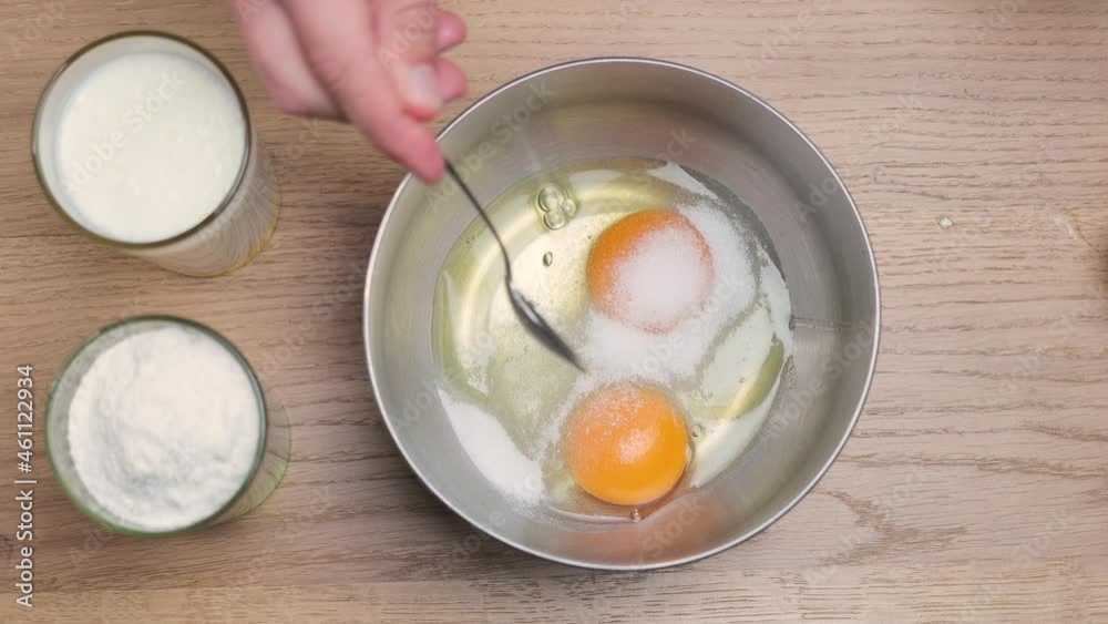 Adding a sugar to the broken chicken eggs in a metal bowl, cooking concept, top view Adding a sugar to the broken chicken eggs in a metal bowl, cooking concept, top view