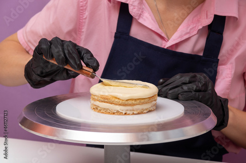 Pastry chef applies cream to layer of bento cake with scraper. Assembly process. Selective focus.
