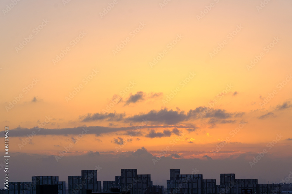 都市の夜明け、早朝ビルの隙間から太陽が昇り辺りはオレンジ色に染まる。ビルはシルエットに浮かぶ