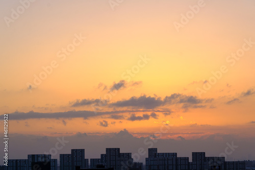  都市の夜明け、早朝ビルの隙間から太陽が昇り辺りはオレンジ色に染まる。ビルはシルエットに浮かぶ