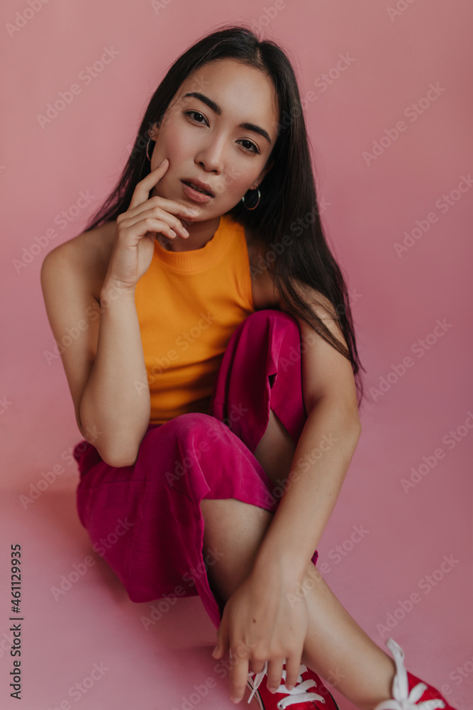 Pale-skinned exotic model looks into camera, meditating and touching her cheeks with hands. Full body studio portrait of adult girl with black long hair wearing colorful outfit. Pale-skinned exotic model looks into camera, meditating and touching her cheeks with hands. Full body studio portrait of adult girl with black long hair wearing colorful outfit.