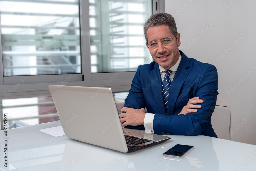 CAUCASIAN BUSINESSMAN WITH FOLDED ARMS AT MODERN OFFICE WITH LAPTOP SMILING AND LOOKING AT CAMERA. CONCEPT OF EXECUTIVE, MANAGER, BOSS, DIRECTOR OR ENTREPENEUR. CAUCASIAN BUSINESSMAN WITH FOLDED ARMS AT MODERN OFFICE WITH LAPTOP SMILING AND LOOKING AT CAMERA. CONCEPT OF EXECUTIVE, MANAGER, BOSS, DIRECTOR OR ENTREPENEUR.