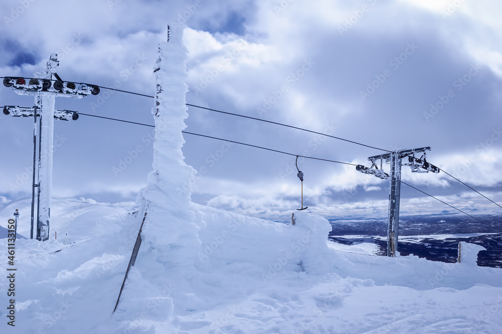 Frozen under strong cold wind snow, ski lift at mountain top, close up photo of ski resort lift equipment