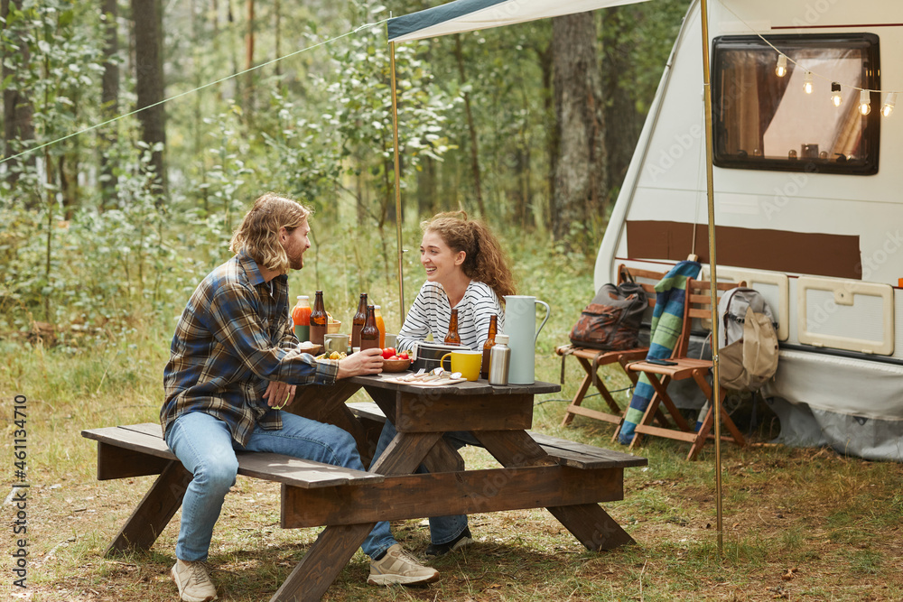 Full length shot of young couple enjoying picnic outdoors while camping with trailer van, copy space Full length shot of young couple enjoying picnic outdoors while camping with trailer van, copy space