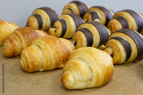 Many classic and chocolate croissants with different flavors are arranged in dense rows on the table. Manual production of handmade croissants and pastries