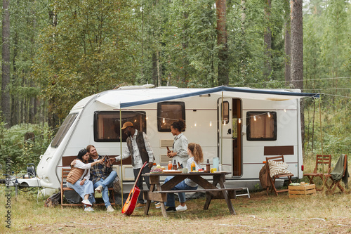 Photographie Wide angle view of young people enjoying outdoors while camping with van in fore