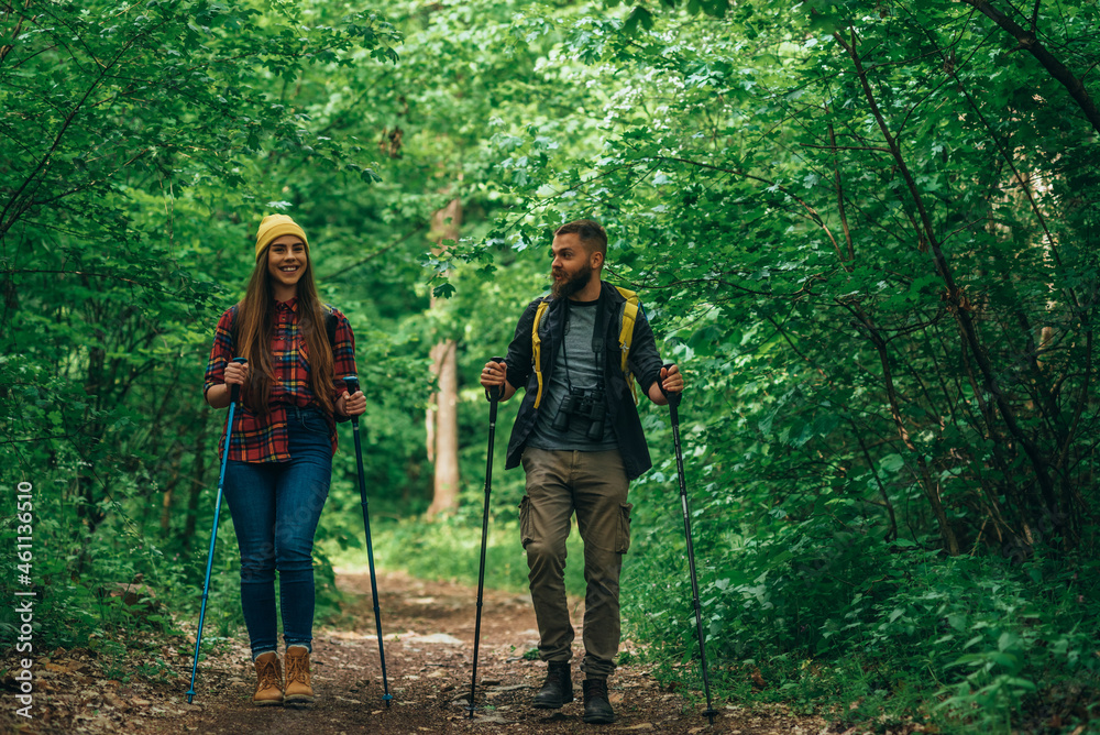 Couple of hikers using trekking poles and wearing backpacks with a camping gear